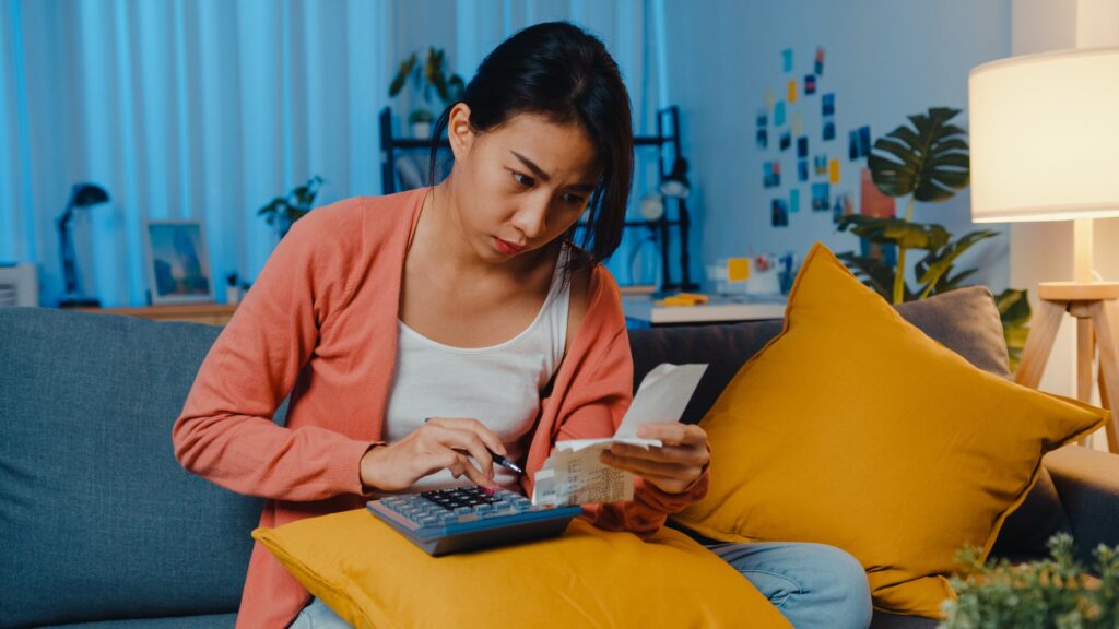 Asian lady feel stress and worried with bill and invoice credit card calculating loan on sofa.